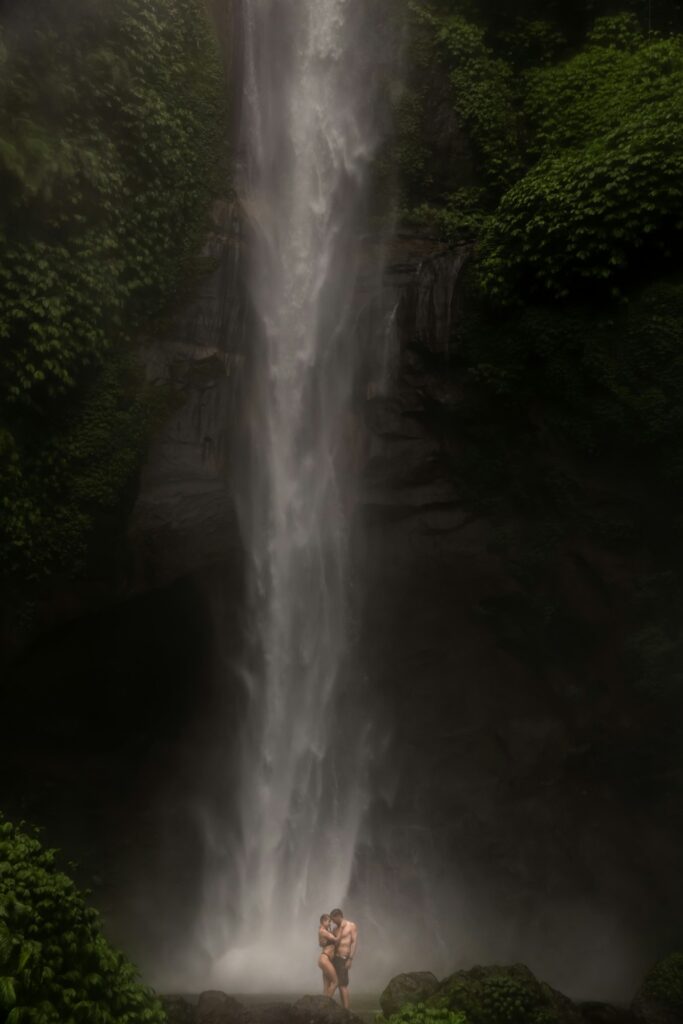 Young couple enjoying the freshness of nature under a waterfall in the tropics.